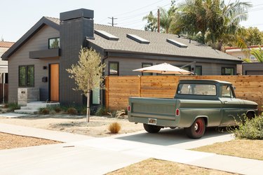 A gray house with a brick chimney, skylights and light wood front door. A green truck is by a wood fence.