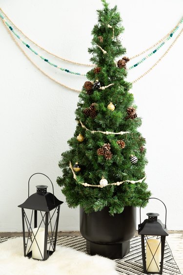 Small DIY Christmas tree with mini ornaments on black and white countertop with lanterns against white wall with decorative hanging bead chains