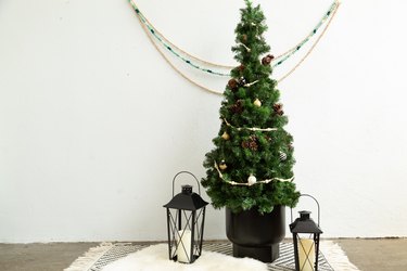 Small DIY Christmas tree with mini ornaments on black and white countertop placemat with lanterns against white wall with decorative hanging bead chains