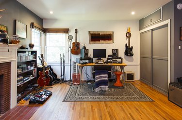 a room with a wood floor and an oriental rug is full of guitars and amplifiers