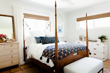 A wood bed post, with blue-neutral bedding, in a bedroom with wood furniture and blue-white decor.