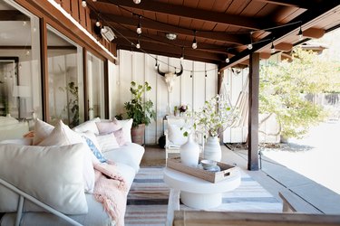 White patio furniture with pink and blue accents, under a wood overhang with string lights.