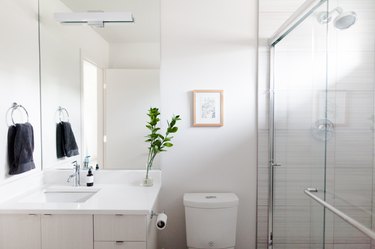 Bathroom with a white vanity, clear vase with a plant clipping, glass door shower, and a flat wall sconce.