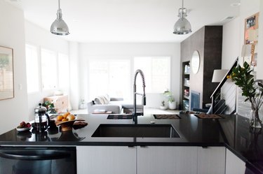 Kitchen with gray pendant lights, over a black-white kitchen island. French coffee press, bowl of oranges, and a clear vase of flowers.