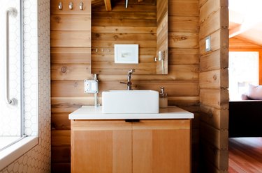 A bathroom with a wood vanity and wood walls. A square sink basin and an arched mirror. A shower with white hexagon tiles.