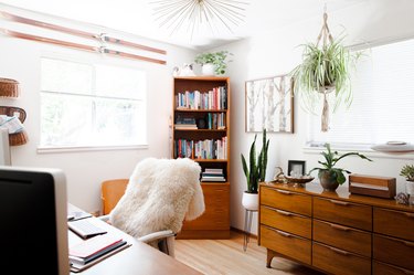 Office with wood furniture, plants, sheepskin throw, and Modernist accents.