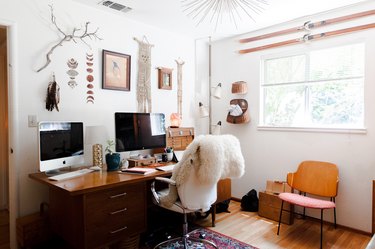 Home office with vintage wood desk, boho wall decor, and nearby window