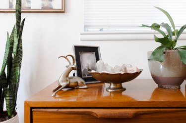 Wood credenza with a silver animal sculpture, framed family photo, a vintage silver bowl of crystals, and plants.