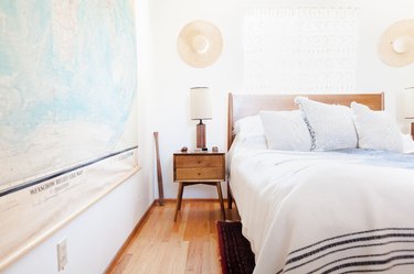 A Wood night stand next to a bed with a wood headboard, in a bedroom decorated with a map and hats.