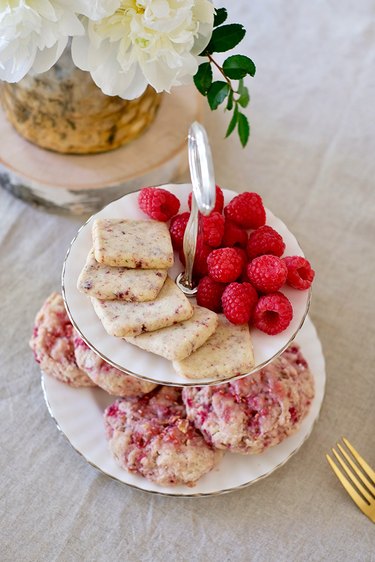 White china dishware with sweets and fruit by vase of flowers on table