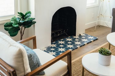 Blue and white star clay tile in front of fireplace. A tree houseplant, white cushioned accent chair, and round coffee table.