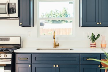 Dark kitchen cabinets with gold handles and white countertop with a single-handle sink and a houseplant