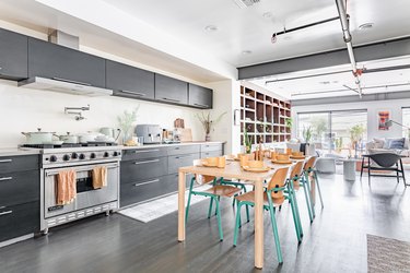 Contemporary kitchen with black cabinets, wood dining table, yellow dishware, turquoise wood frame chairs