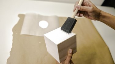 applying white paint to a block of wood with a foam brush