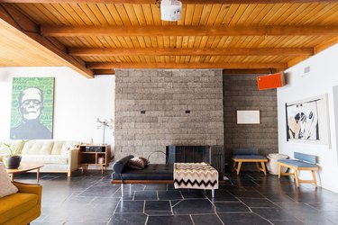 Living room with midcentury furniture, pop art, natural black tile floor, concrete brick wall, and wood beam ceiling.