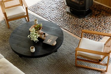 Two wood-cane accent chairs on a gray rug, with a round black coffee table. A stove fireplace and a stone hearth.