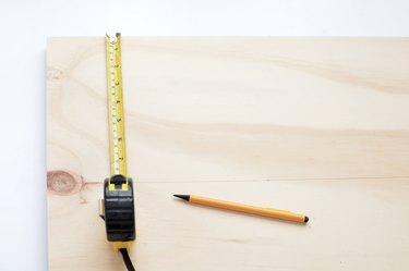 using a tape measure and pencil to mark where moulding will go on a plywood sheet