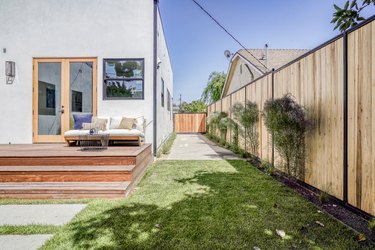 Modern gray house with varying window sizes and casement door. A wood deck with seating. A wood fence with plants.