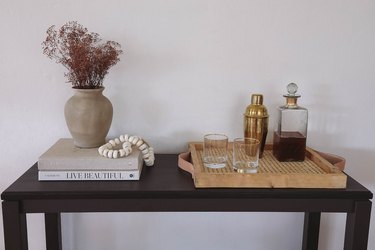 Wood, cane, and leather handle bar tray with a crystal decanter, drinking glasses, shaker, and on top of a table