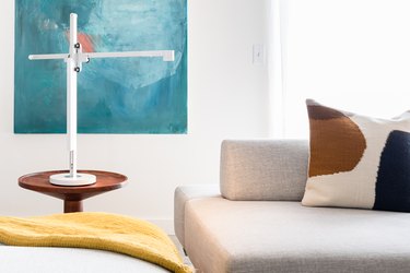White industrial lamp on wood side table with painting and gray sofa with pillow