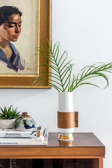 a vase with a decorative diy leather wrap sitting on a tabletop and filled with greenery