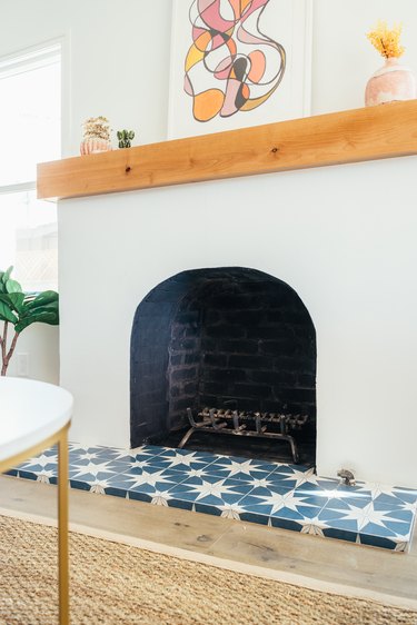 Blue and white star clay tile in front of fireplace. Wood mantel with contemporary art and vases with plants.