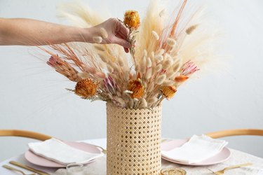 Cane vase with dried flowers and grass on dining table.