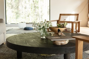 Dark round wood coffee table with a vase of flowers and accent pottery, and wood-cane chairs.