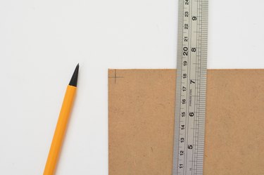 Metal ruler laying flat on top of cardboard panel next to mechanical pencil against a white background