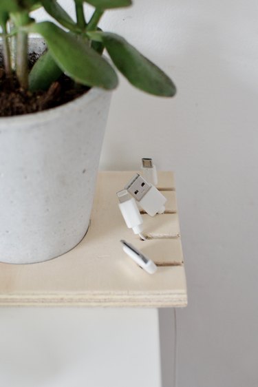 close-up on a cable organizer made out of a square of plywood with cables hanging from it and a potted plant inset