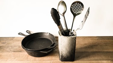 Utensils in concrete vase next to black cast-iron pans on wood counter