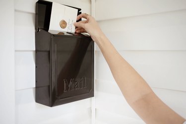 Person putting a piece of mail with a gold wax seal into a black mailbox