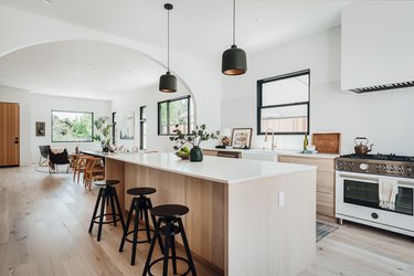 White counter and wood base kitchen island with black stools and black pendant lights above.