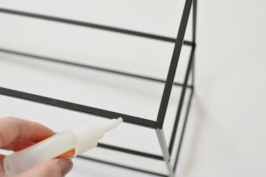Hand applying Gorilla Glue to a black metal shelving frame against a white background