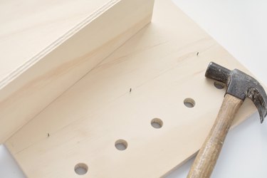 a hammer lies on a sheet of plywood with holes drilled in it and nails sticking through from the other side