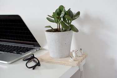 a cable organizer made out of a square of plywood with cables hanging from it and a potted plant inset