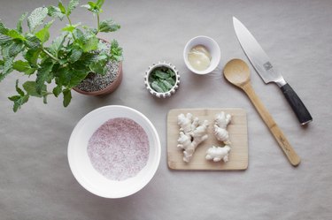 ginger root on a cutting board surrounded by bowls of mint, salt, and glycerine