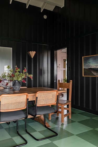 Black wall paneled dining room with a green checkerboard floor, eclectic furniture and decor.