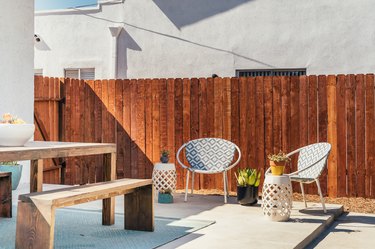 A wood fence by two round patio chairs with porcelain lace side tables and wood picnic table-bench set.