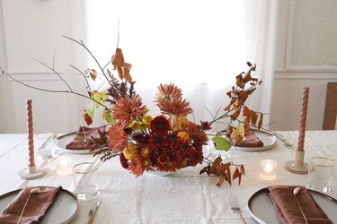 Dining table with brown accents and a flower arrangement of red and pink flowers and branches of leaves