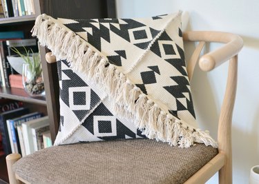 Black and white fringed pillow on chair next to bookcase