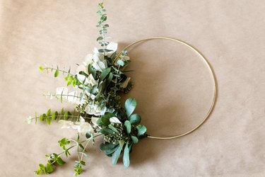 DIY Christmas decorations with bunches of greenery and white seed pods attached to a wire hoop