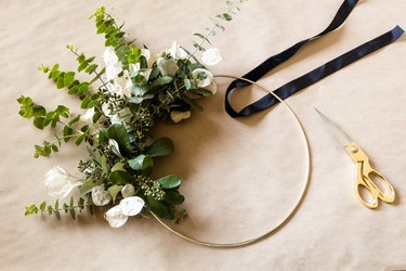 preparing to attach a ribbon to a diy wreath wrapped around a gold hoop
