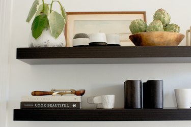 Dark shelves with black and white dish ware, cookbooks, plant in a vase, and wood bowl of artichokes