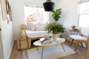 Living room with Black pendant light, oval white coffee table with a vase of flowers and books, rattan bench, white pillows