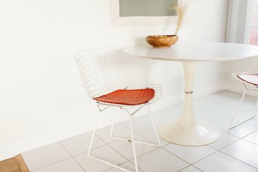 White tulip table and bertoia chairs with burnt orange cushions in white kitchen