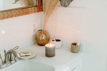 White tiled bathroom counter with lit candle and ceramic cups