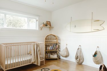 Neutral wood and white wainscoting nursery with white surfboard and baskets hanging on walls