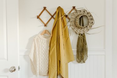 Coat rack with white sweater, yellow jacket and palm weaved hat hanging