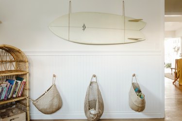 White wainscoting wall with surfboard hanging above with neutral baskets hanging